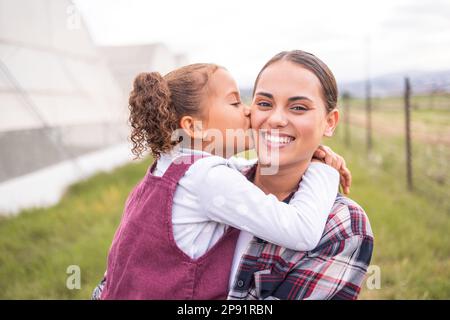 Mutter, Kuss und Mädchen auf einer Farm für Nachhaltigkeit, Landwirtschaft und Ökologie mit Liebe und Fürsorge für die Familie. Porträt einer Mama und Kind auf einem umweltfreundlichen, sauber Stockfoto