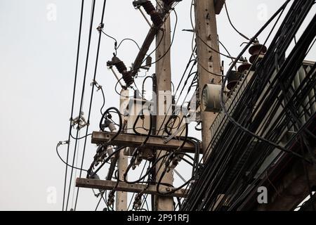 Einige Strommasten, komplizierte Drähte und eine Menge Telefonkabel gegen den grauen Himmel. Viele chaotische Elektro- und Telefonkabel in einer thailändischen Stadt Stockfoto