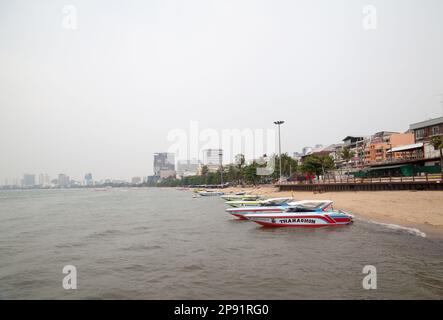 Pattaya, Thailand - 28. März 2016: Farbenfrohe Boote am Strand an einem wolkigen nebligen Tag. Seascape mit Gebäuden am Horizont und grauem Himmel Stockfoto