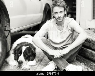 Süßes Porträt eines gutaussehenden Erwachsenen, der draußen neben seinem Hund, einem Sankt Bernard, chillt. Das Bild ist schwarz-weiß. Stockfoto