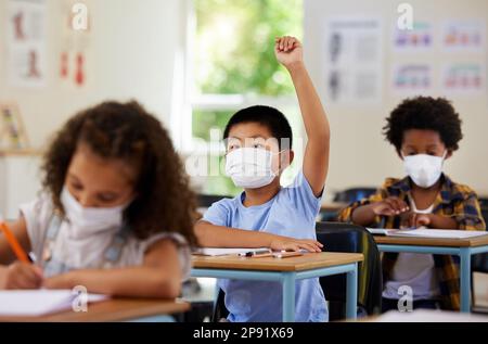 Schüler heben die Hand, um sich freiwillig zu melden, teilzunehmen und Fragen im Unterricht in covid Pandemie zu beantworten. Neugieriger, intelligenter und kluger Junge Stockfoto