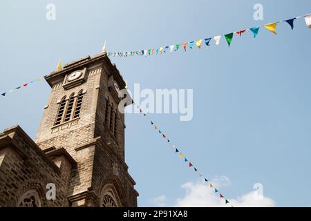 Alte katholische Kirche Turm mit einer Uhr, mit bunten Fahnen dekoriert. Historische gotische Architektur in einer Stadt von Nha Trang, Vietnam Stockfoto
