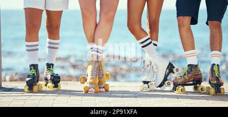 Rollschuhe, Freunde und Strand mit einer Gruppe von Menschen auf der Promenade am Strand mit dem Meer im Hintergrund. Sommer, Spaß und Lifestyle mit einem Stockfoto