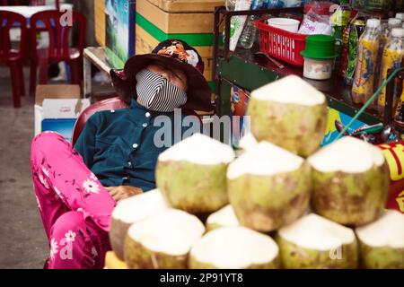 Nha Trang, Vietnam - April 1, 2018: Vietnamesische Street Food vendor am Arbeitsplatz schlafen. Müde Asiatische Dame verkauft Kokosnüsse auf dem Markt Stockfoto