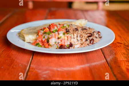 Traditionelles Gallo Pinto-Gericht mit Pico de Gallo und Quesillo, Gallopinto-Gericht mit Quesillo und Pico de gallo auf einem Holztisch Stockfoto