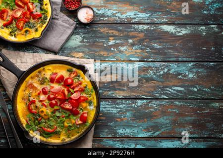 Gesunde Frittata in zwei gusseisernen Pfannen mit gebratenen Eiern und Gemüse der Saison auf rustikalem Holzhintergrund. Italienisches Omelette mit Bio-Omelette Stockfoto