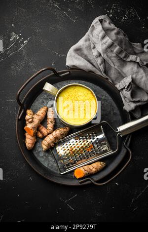 Gesundes warmes Getränk zur Stärkung des Immunsystems, Kurkuma goldene Milch. Zutaten zum Kochen von Detox Curcuma Milch in rustikalem Blechbecher, frischer Kurkuma Stockfoto