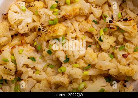 Nahaufnahme von gebackenem Blumenkohl mit Kräutern in weißer Keramikschale, Draufsicht. Vegetarische gesunde Lebensmittel, sauberes Essen Konzept Hintergrund Stockfoto