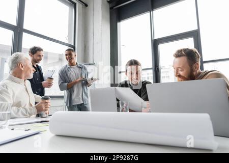 Gemischtrassige Geschäftsleute, die Kaffee trinken und Laptops während des Meetings im Büro benutzen, Bestandsbild Stockfoto