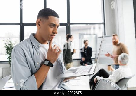 Fokussierter afroamerikanischer Geschäftsmann, der während der Arbeit im Büro auf ein Notebook schaut, Bild von Stock Stockfoto