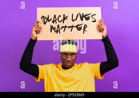 Schwarzer ethnischer Mann in gelber Kleidung auf lila Hintergrund, zeigt mit einem Schild, schwarze Leben sind wichtig, wütend Stockfoto
