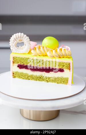 Ein Stück Pistazienkuchen mit Sahne- und Erdbeerfüllung, dekoriert mit Schokolade, Baiser, Süßigkeiten Stockfoto