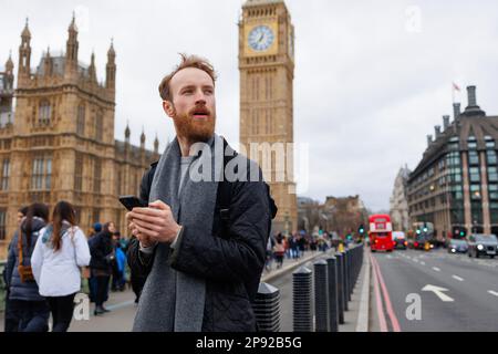 Ein überraschter Mann, der in der Londoner Straße ein Smartphone benutzt Stockfoto