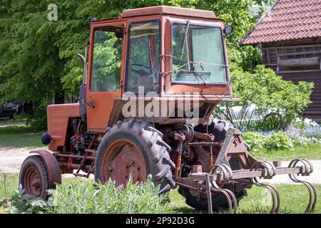 Alter Landwirtschaftstraktor in Orange auf grünem Gartenhintergrund Stockfoto