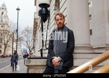 Ein Mann mit Bart, stilvoll gekleidet, in einer Jacke und einem Schal in der Nähe eines wunderschönen alten Gebäudes in den Straßen Londons Stockfoto