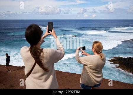 Weibliche Touristen fotografieren mit ihren Telefonen auf dem beliebten Aussichtspfad mirador el golfo Küstenaussichtspfad Lanzarote, Kanarische Inseln, Spanien Stockfoto