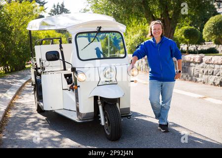 Porträt einer Fahrerin eines Tuk-Tuk-Elektroautos. Führen und fahren Sie mit umweltfreundlichen Transportmitteln in der Altstadt. Tourismusarbeiter in Helsinki Stockfoto