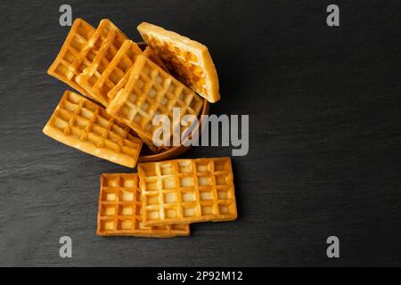 Belgische Waffel isoliert, quadratische Waffel in Wood Bowl, hausgemachte weiche goldene belgische Waffeln, Wafer Biscuit Frühstück auf schwarzem Hintergrund Stockfoto