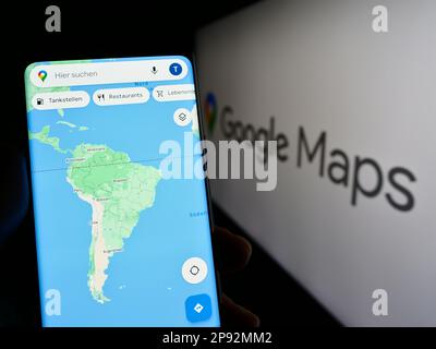 Person, die ein Mobiltelefon mit einer Webseite der Web-Mapping-Plattform Google Maps auf dem Bildschirm vor dem Logo hält. Konzentrieren Sie sich auf die Mitte des Telefondisplays. Stockfoto