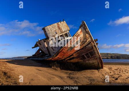 Historisches Fischerboot-Wrack aus Holz am Sandstrand in der Sonne und am blauen Himmel Stockfoto