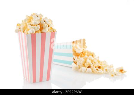 Zwei pinkfarbene und blau-weiß gestreifte Eimer mit leckerem Käsepopcorn, isoliert auf weißem Hintergrund. Schachtel mit Streuung von Popcornkörnern. Filme, Stockfoto