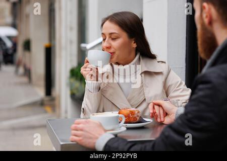 Ein Paar, das gerne frühstückt, Kaffee und einen Donut an einem Tisch im Café serviert und Händchen hält Stockfoto