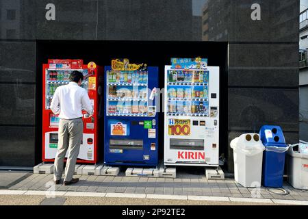 Ein Mann, der Getränke aus einer Reihe von Verkaufsautomaten entlang der Straße von Tokio einkauft - Straßenszene in Tokio - Japan Stockfoto