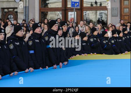 Lemberg, Ukraine. 10. März 2023. Polizisten singen die Nationalhymne, während sie eine riesige ukrainische Flagge vor dem Rathaus Ratusha hielten, zu Ehren des Jahrestags der ersten Aufführung der Nationalhymne vor 158 Jahren. (Foto: Mykola Tys/SOPA Images/Sipa USA) Guthaben: SIPA USA/Alamy Live News Stockfoto