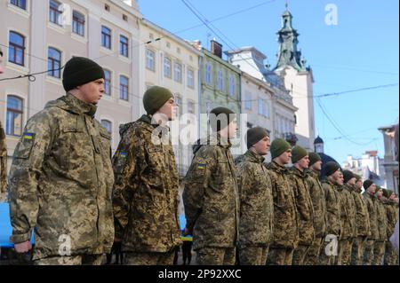 Lemberg, Ukraine. 10. März 2023. Militärpersonal singt die Nationalhymne, während es vor dem Rathaus Ratusha eine große ukrainische Flagge hält, um den Jahrestag der ersten Aufführung der Nationalhymne vor 158 Jahren zu feiern. (Foto: Mykola Tys/SOPA Images/Sipa USA) Guthaben: SIPA USA/Alamy Live News Stockfoto