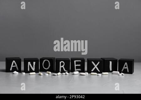 Das Wort "Anorexia" besteht aus Würfeln mit kreideförmigen Buchstaben neben Pillen auf einem beleuchteten Tisch Stockfoto