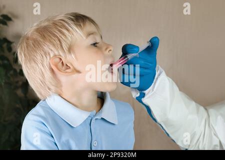 Der Junge bekommt Polio-Tropfen. Arztmachen zum Kind orale Schutzimpfung gegen Infektionen. Kleiner blonder Haarjunge im Krankenhaus. Kindergesundheitsfürsorge und Kinderkrankheiten Stockfoto