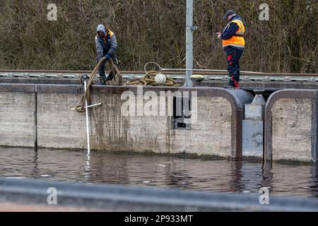 10. März 2023, Bayern, Wörth an der Donau: Arbeiter entfernen das Flotsam aus der Geisling-Schleuse, wo zuvor ein etwa 80 Meter langes und mit Eisenerz beladenes Frachtschiff in der Donau gesunken war. Nach ersten Berichten wurden zwei Personen an Bord unverletzt, aber als Vorsichtsmaßnahme ins Krankenhaus gebracht. Die Ursache für den Untergang des Schiffes blieb zunächst unklar. Foto: Armin Weigel/dpa Stockfoto