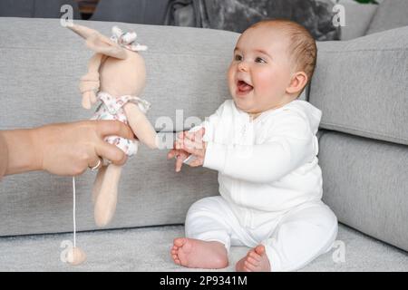 Mutter schenkt ihrer kleinen Tochter Spielzeug, spielt mit einem kleinen Mädchen, mutter genießt während des Mutterschaftsurlaubs Kinderbetreuung, sitzt im Bett im Schlafzimmer bei Ho Stockfoto