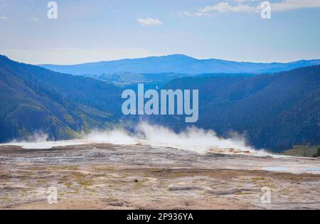 Im Yellowstone-Nationalpark erhebt sich Dampf aus einer heißen Quelle vor einer blauen Berglandschaft Stockfoto