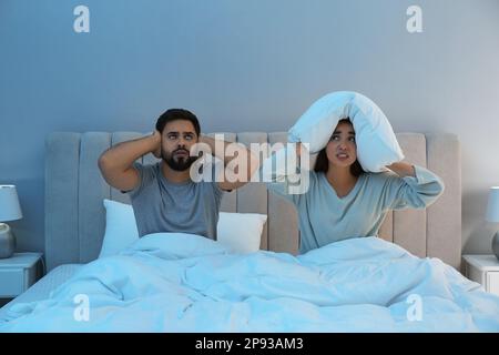 Ein junges Paar, das von lauten Nachbarn im Bett zu Hause gelitten hat Stockfoto