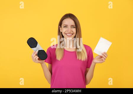 Glückliche junge Frau mit Einweg- und wiederverwendbaren Stoffeinlagen auf gelbem Hintergrund Stockfoto