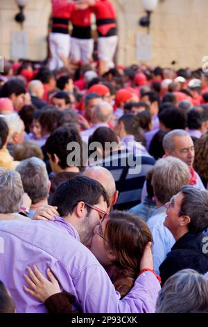 Ein paar Küsse von Colla Jove Xiquets de Tarragona. Im Hintergrund bauen die 'Castellers' den menschlichen Turm, eine katalanische Tradition. Fira de Santa Teresa, Stadtfest Stockfoto