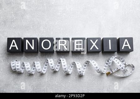 Word Anorexia aus Würfeln mit Buchstaben in der Nähe des Maßbandes auf einem leichten Tisch, flach liegend Stockfoto