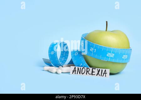 Papier mit Wort Anorexie, Apfel, Maßband und Pillen auf hellblauem Hintergrund Stockfoto