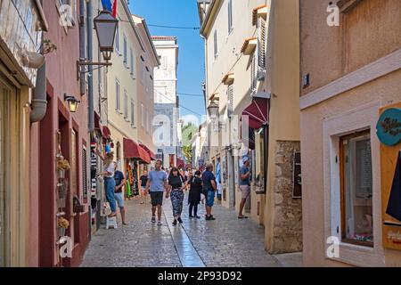 Touristen, die in einer Gasse mit Geschäften in der historischen Altstadt von Krk, Primorje-Gorski Kotar County, Kroatien, spazieren gehen Stockfoto