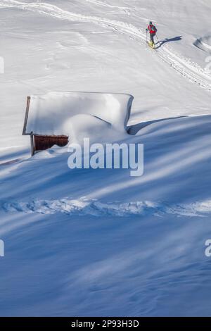 Italien, Veneto, Provinz Belluno, Livinallongo del Col di Lana, Bergsteiger bergauf Richtung Sief Saddle, vorbei an einer schneebedeckten Holzhütte, Dolomiten Stockfoto