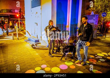 Tel Aviv, Israel. 10. März 2023. Ein israelischer Mann führt seinen Hund neben einer bewaffneten Grenzpolizistin an einer Kreuzung nach einem Schussangriff auf die Dizingof Street. Die militante palästinensische Gruppe Hamas hat sich für den Terroranschlag in Tel Aviv am Donnerstagabend verantwortlich gemacht, bei dem drei Israelis verletzt wurden. Der Angriff im Herzen der Stadt erfolgte nach einem Tag des Protests der israelischen Opposition gegen Netanjahus Regierung. Kredit: SOPA Images Limited/Alamy Live News Stockfoto