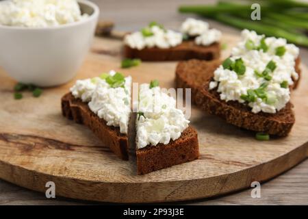 Brot mit Hüttenkäse und grünen Zwiebeln auf Holztisch, Nahaufnahme Stockfoto