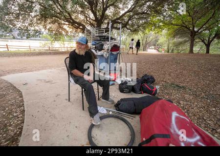 Ein Obdachloser, der nicht identifiziert werden wollte, sitzt am 9. März 2023 bei den meisten seiner Sachen auf dem Wander- und Radweg entlang der Nordküste des Lady Bird Lake in der Innenstadt von Austin. Der Mann, der seit etwa 9 Monaten an der Küste zeltet, wurde schließlich von Crews gebeten, zu gehen, die einen geteilten Zaun bauen und Beleuchtung hinzufügen, nachdem er kürzlich ertrunken war. ©Bob Daemmrich Stockfoto