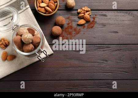 Verschiedene leckere vegane Bonbonbälle und Nüsse auf Holztisch, flach liegend. Platz für Text Stockfoto