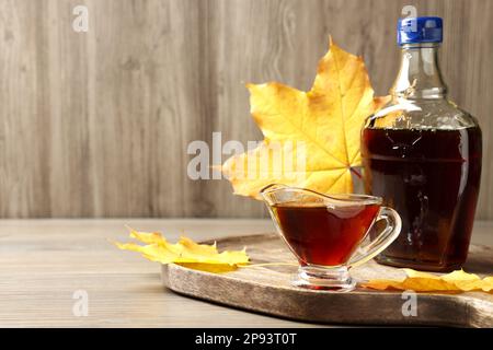 Flasche und Sauce mit leckerem Ahornsirup auf einem Holztisch, Platz für Text Stockfoto