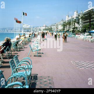 1960er, historisch, Blick entlang der berühmten Promenade des Anglais, Nizza, Frankreich, langer, ruhiger Fußweg mit Blick auf das Mittelmeer an der französischen Riviera. Auf dem Bild ist ein Schild für das Restaurant Ruhl Plage am kleinen öffentlichen Strand zu sehen. Es wurde 1920 eröffnet und ist das älteste Strandrestaurant in Nizza, das vom Eigentümer geführt wird. Ein weiteres Schild ist für das Plage du Festival. Stockfoto