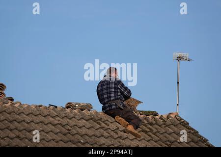 Ein Dachdecker, der Kammfliesen auf dem Dach eines Hauses repariert Stockfoto