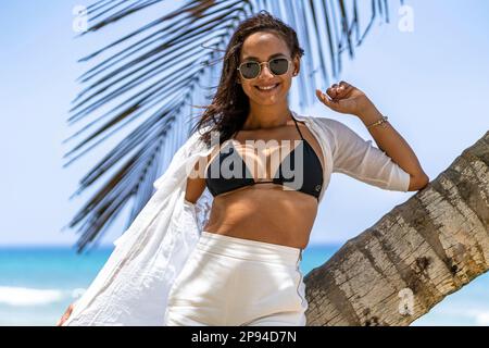 Nordamerika, Karibik, Großantillen, Hispaniola, Dominikanische Republik, Provinz Puerto Plata, Cabarete, attraktive Frau, die sich gegen eine Palme am Strand lehnt Stockfoto