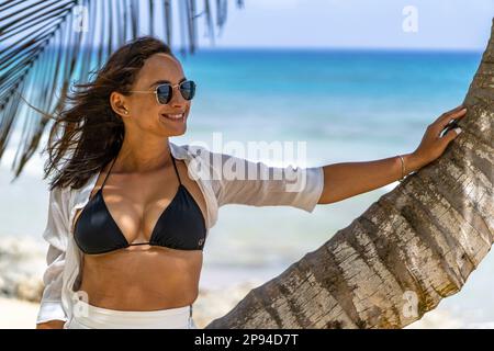 Nordamerika, Karibik, Großantillen, Hispaniola, Dominikanische Republik, Provinz Puerto Plata, Cabarete, attraktive Frau, die sich gegen eine Palme am Strand lehnt Stockfoto